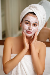 Woman with towel is applying mask on her face at home, close-up. Skin care.