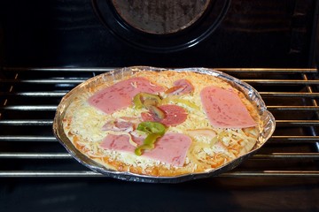 Precooked frozen pizza in aluminum dish placed in electric oven to bake 