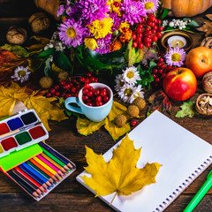 notebook and stationery, paint pencils on a background of autumn flowers and leaves