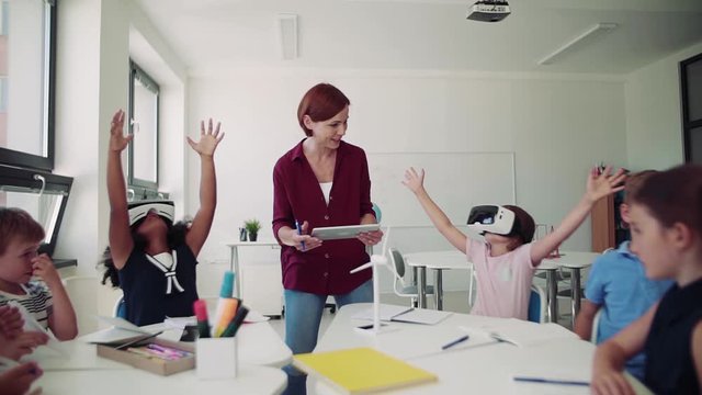 A group of small school kids with VR goggles and teacher in class, learning.