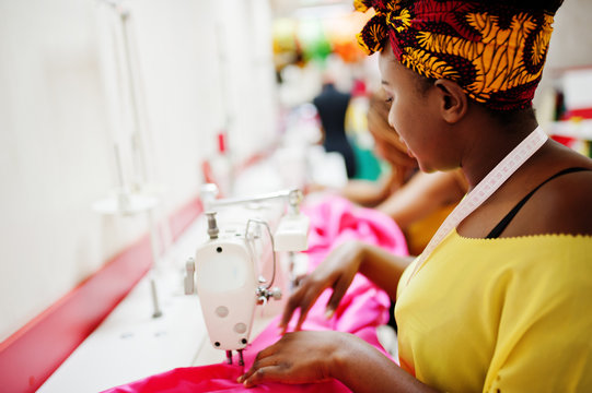 Two african dressmaker woman sews clothes on sewing machine at tailor office. Black seamstress girls.
