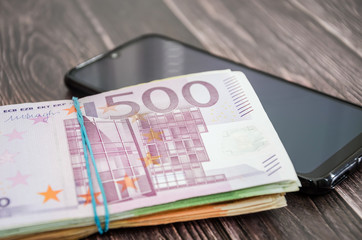 black phone and euro banknotes on a wooden background.