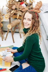 Charming woman in green wool sweater wrapping presents for Christmas celebration