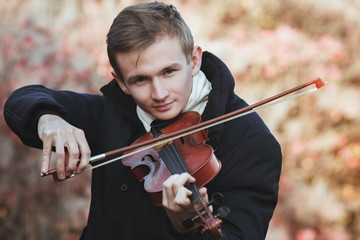 portrait of a young elegant man playing the violin on autumn nature backgroung, a boy with a bowed...