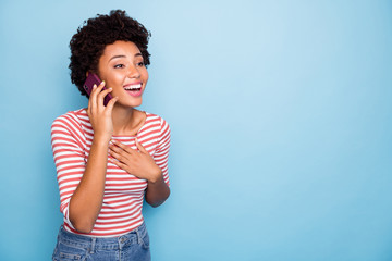 Photo of beautiful crazy dark skin wavy lady hold telephone speaking with best friend listen humorous story wear casual striped sweater jeans isolated blue color background