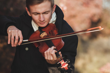 portrait of a young elegant man playing the violin on autumn nature backgroung, a boy with a bowed...