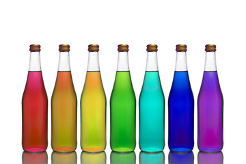 Transparent glass bottles of different colors stand on a mirror surface on a white background making up an owl rainbow.