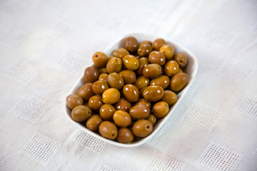 Green olives in white plates lined up on white tablecloth Preserved in olive oil, used as table olives.  