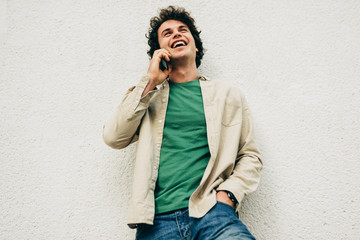 Outdoor portrait of young man talking on mobile phone with his friend. Happy male with curly hair...
