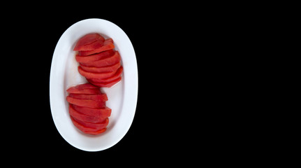 Sliced and peeled tomatoes in white plate. Plate to the left of the black background 