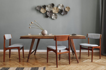 Modern and stylish dining room interior with glamour wooden table , elegant chairs and design decoration. Template. Home decor. Gray background wall. 