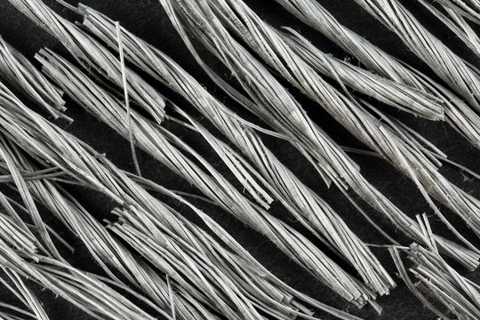 Extreme close up, top down view of bundels of grey colored, twisted polypropylene macro fibers for concrete reinforcement on black stone background