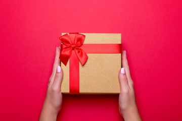 Woman manicured hands holding red and golden wrapped present or gift box on deep red background, copy space, top view, flat lay. Background for Valentine's Day, Mother's Day.