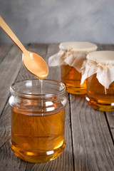 Pouring aromatic honey into jar, closeup. Honey in glass jars and honeycombs wax on wooden background. Wooden stick , instruments