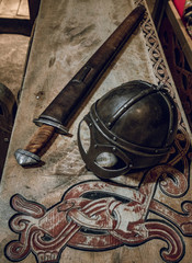 Viking helmet and viking sword on wooden table with wood carvings.