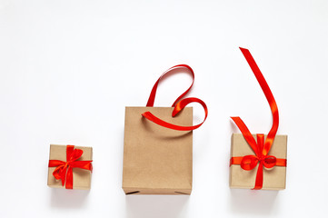 Three gifts wrapped in boxes and bag of craft paper and tied with red satin ribbon on white background. Eco packaging. Festive composition, sale, shopping. Place for text, flat lay, close up, mock up
