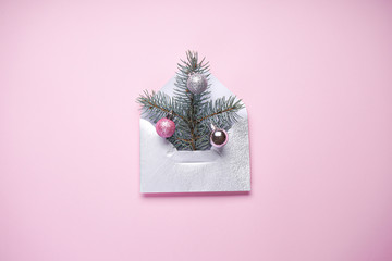Christmas composition. Christmas tree in the envelope, the minimum Christmas card, fir branch with colored Christmas balls on a pink background. Flat lay.
