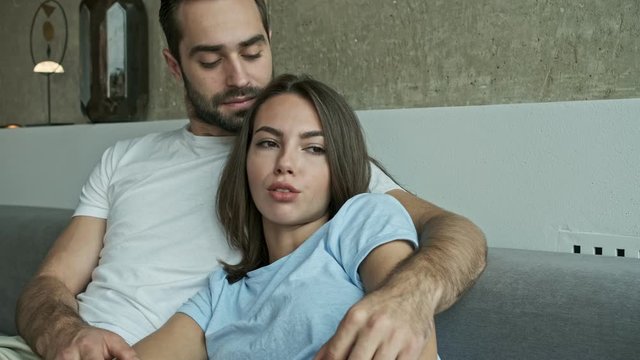 Close up view of cute serious young lovely couple hugging and speaking while sitting on couch at home