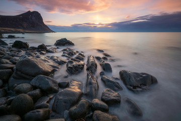 Fototapeta na wymiar Long exposure shot in Myrland/Lofoten islands in Norway. Wet stones infront and sunset and mountains as backdrop.