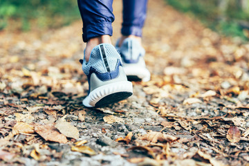 Close up of legs in runner sneakers on track with fallen autumn leaves.