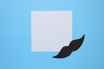 Black paper moustache and writing paper sticker on a blue background. The concept of awareness of men's health and prostate cancer. Space for text