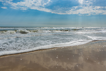 Waves on the beach under the rays of the sun reaching through a blue sky