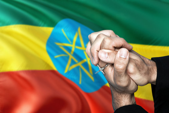 Ethiopia flag and praying patriot man with crossed hands. Holding cross, hoping and wishing.