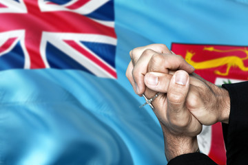 Fiji flag and praying patriot man with crossed hands. Holding cross, hoping and wishing.