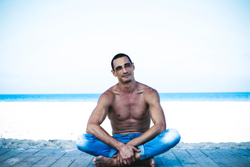 young muscular man in denim pants resting and posing on the beach