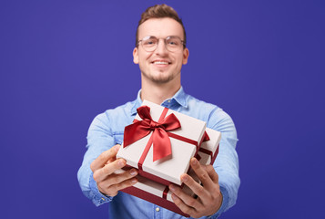 Cheerful guy in blue denim shirt and round glasses giving you gift