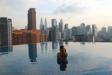 Young happy girl swimming alone in the infinity pool on rooftop in Kuala Lumpur in Malaysia.