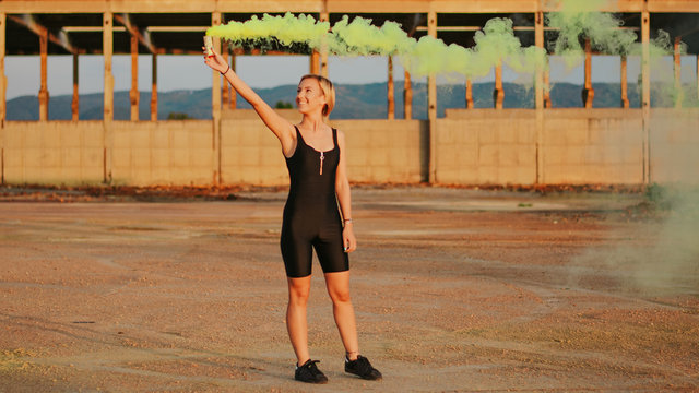 happy young woman having fun with colorful powder cloud. girl running with yellow color smoke bomb