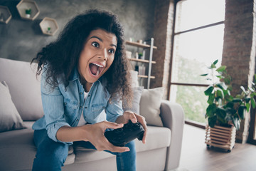 Closeup photo of pretty dark skin wavy lady hold gamepad console joystick addicted gamer worried excited sitting comfy couch casual denim outfit living room indoors