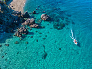 Aerial view of a motor boat sailing near the rocks and the beach of Tropea, Calabria, Italy