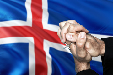Iceland flag and praying patriot man with crossed hands. Holding cross, hoping and wishing.