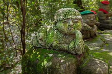 Snake - symbol of japanese horoscope. Childish Jizo stone statue wearing knitted and cloth hats with zodiac animal.