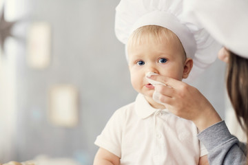 mother and child on kitchen, white hats of chef, mom wipes baby with help of napkin