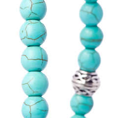 Closeup of a bracelet of turquoise pearls with tibetan metal spacer on a white background