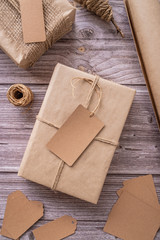 Gift boxes wrapped in craft paper with tags and labels on wooden background top view flat lay