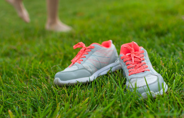 Gray sneakers lying on green grass over background of a child's legs enjoyng barefooted walking.