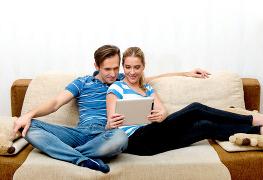Couple Enjoying Of Watching Streaming Media On Tablet While Sitting On Sofa.