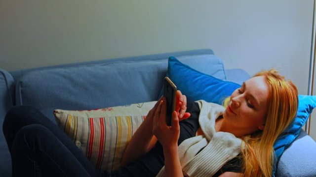Happy young woman lying on sofa and texing sms or other massage on smartphone.