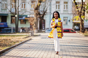 Stylish african american women in yellow jacket posed on street at sunny day with mobile phone at hand.