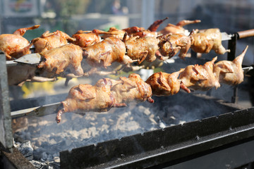 Grilled chickens on a spit. Rotisserie chicken. Brazier and coals.