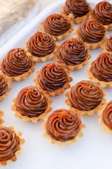 Many appetizing tartlets, cake basket with brown cream on a white tray. Summer dessert.