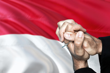Monaco flag and praying patriot man with crossed hands. Holding cross, hoping and wishing.