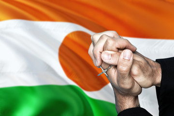 Niger flag and praying patriot man with crossed hands. Holding cross, hoping and wishing.
