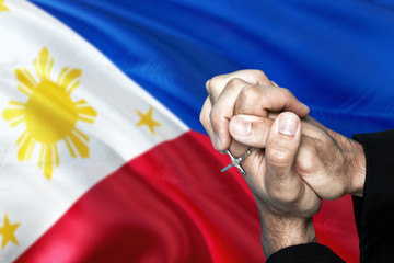 Philippines flag and praying patriot man with crossed hands. Holding cross, hoping and wishing.