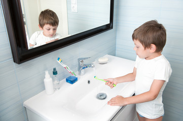 Fototapeta premium healthy little caucasian boy in white shirt washing toothbrush under water in blue bathroom with mirror