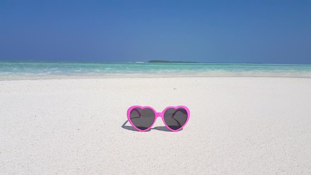 pink heart Sunglasses on a white sandy beach in the Bahamas, Calm ocean waves on sand from Ocean lagoon